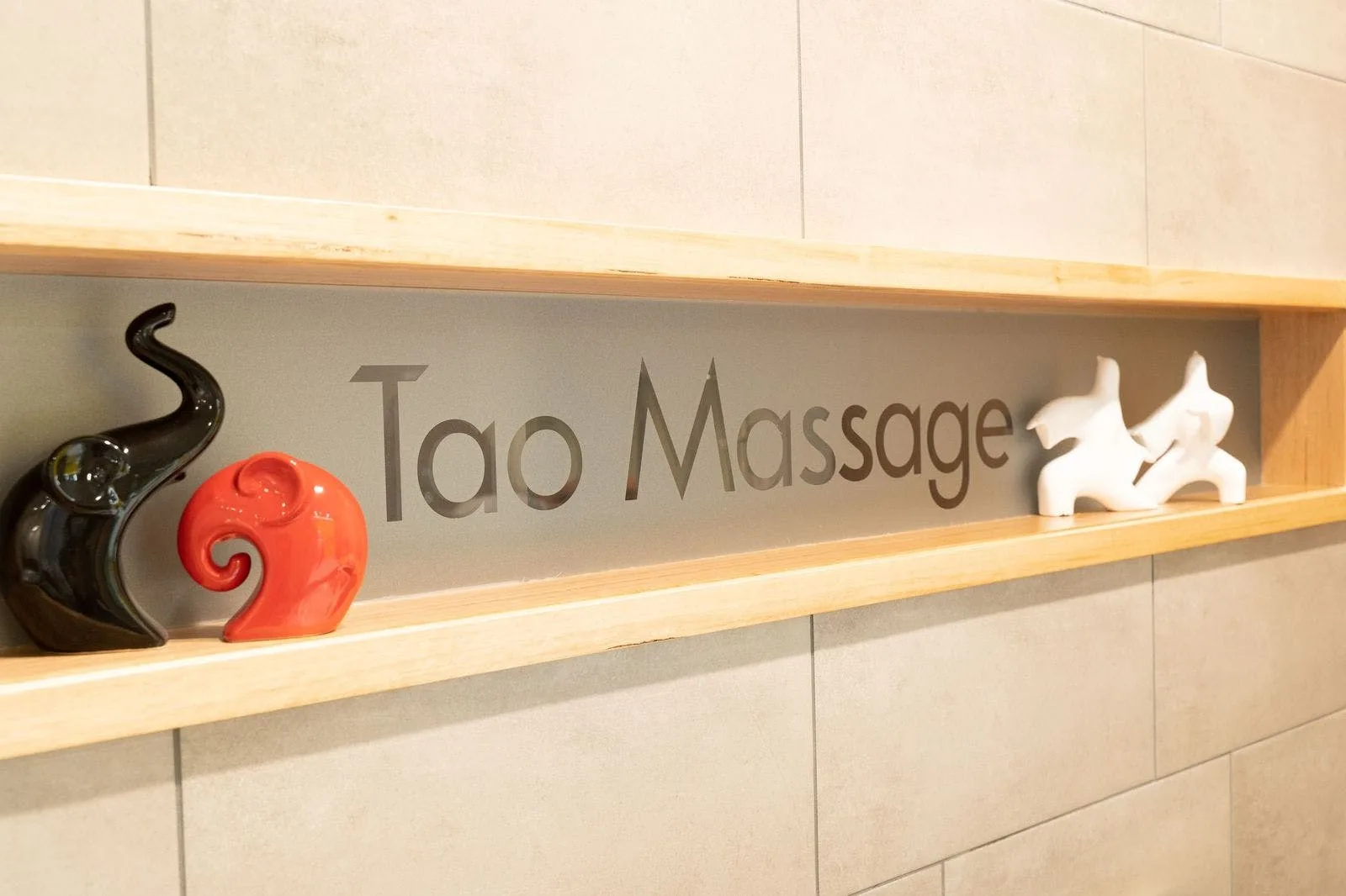 Reception niche — recessed wood-framed shelf holding the frosted TAO Massage sign, flanked by ceramic elephants