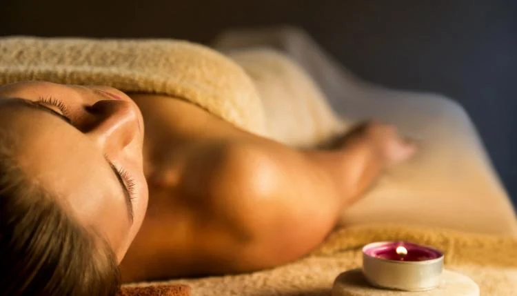 Person resting during a massage session beside a lit candle in warm low light